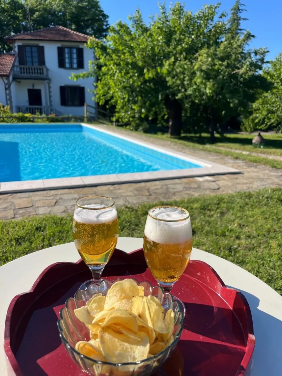 Poolside with the house behind, drinks and snacks on a tray