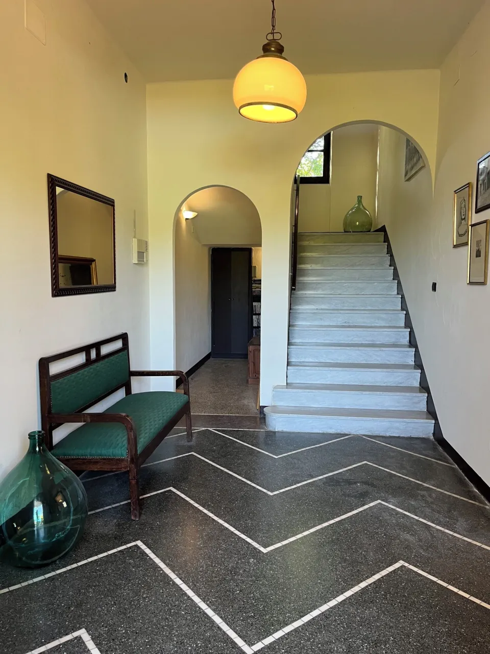 Hallway with a green sofa, large mirror and patterned floor